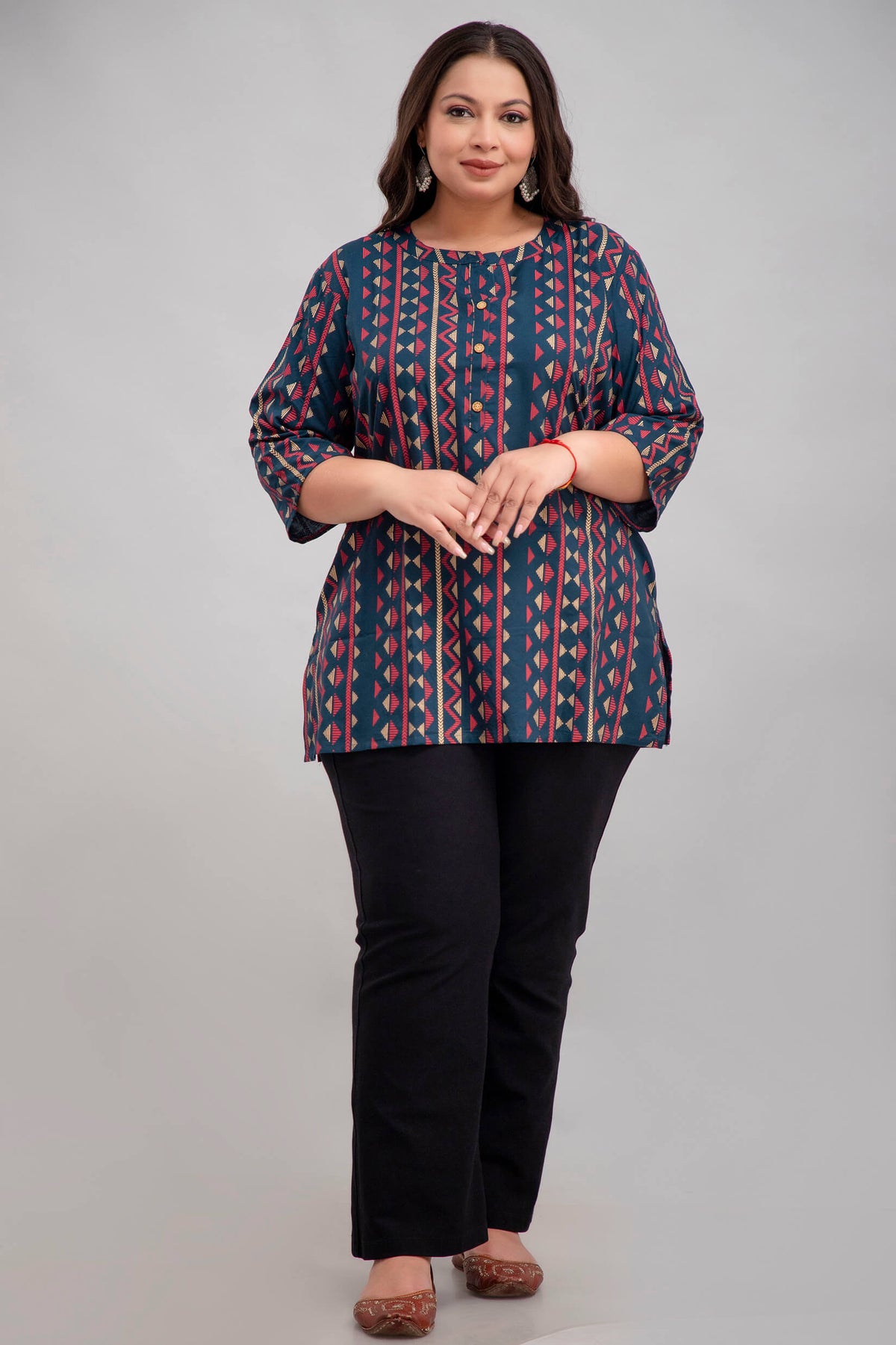 Woman wearing a patterned plus size short kurti tunic and black pants on a gray background