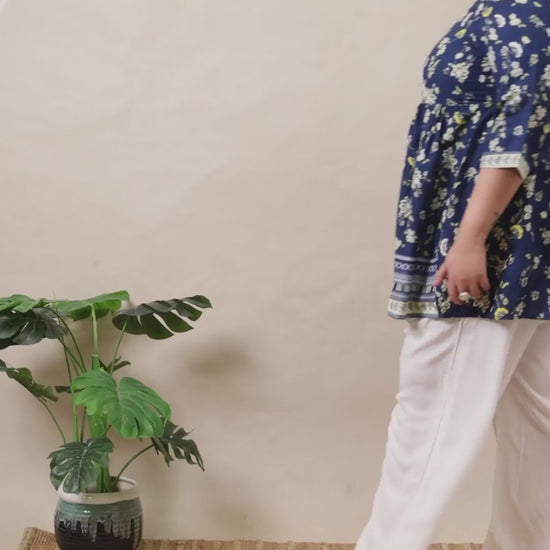 Plus size blue floral wrap tunic by Curvisha styled with white trousers for a flattering silhouette.