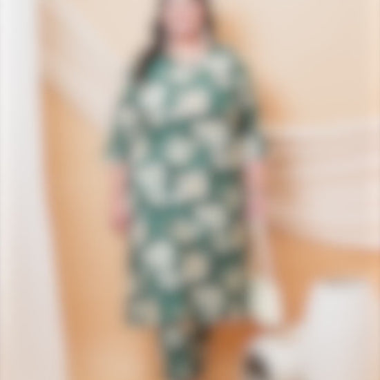 Plus-size model wearing an emerald green floral co-ord set with a V-neck tunic and matching trousers, styled with a white handbag.